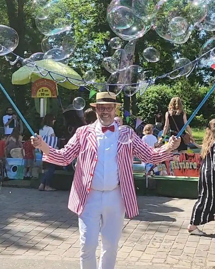 Dans un parc, Rigadin en canotier et veste rayée, au milieu des bulles géantes