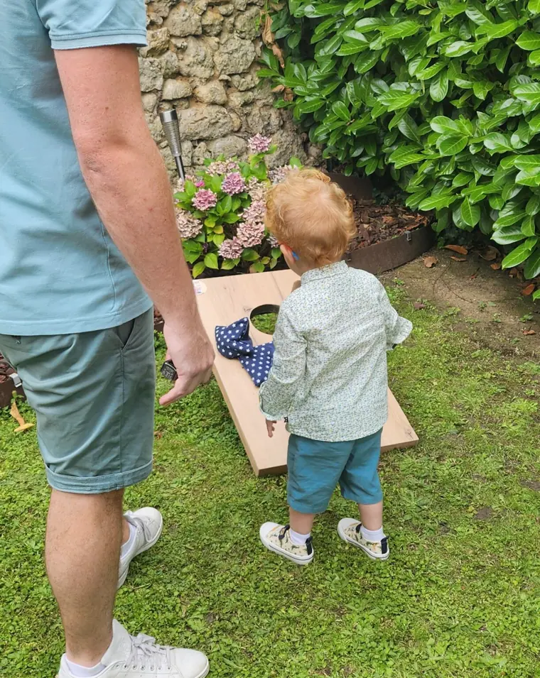 Un père et son jeune fils jouent à un jeu de lancer en bois dans un jardin
