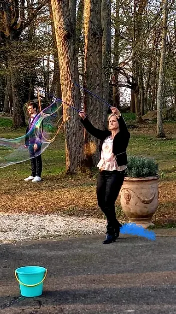 Dans un parc, une invitée fait une bulle géante, un seau bleu à ses pieds