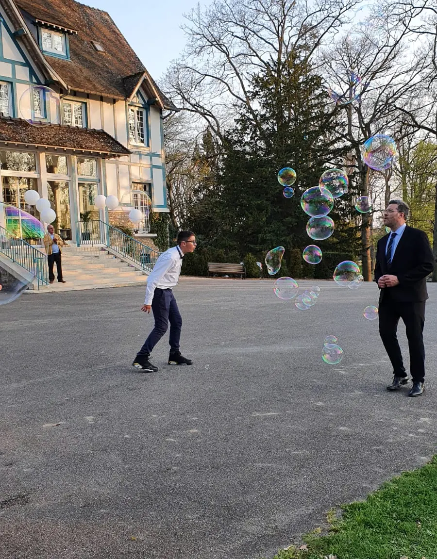 Des bulles géantes s’envolent devant une grande maison, sous le regard des invités