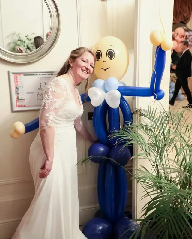 Une mariée pose à côté d’un grand personnage sculpté en ballons bleus