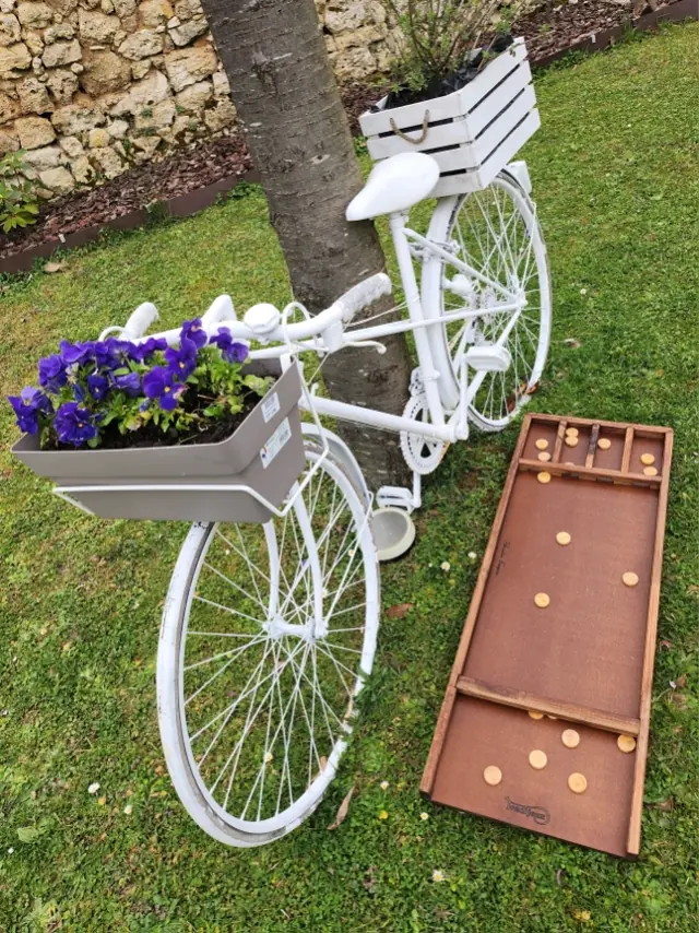 Un jeu de palets en bois posé dans l’herbe à côté d’un vélo blanc fleuri