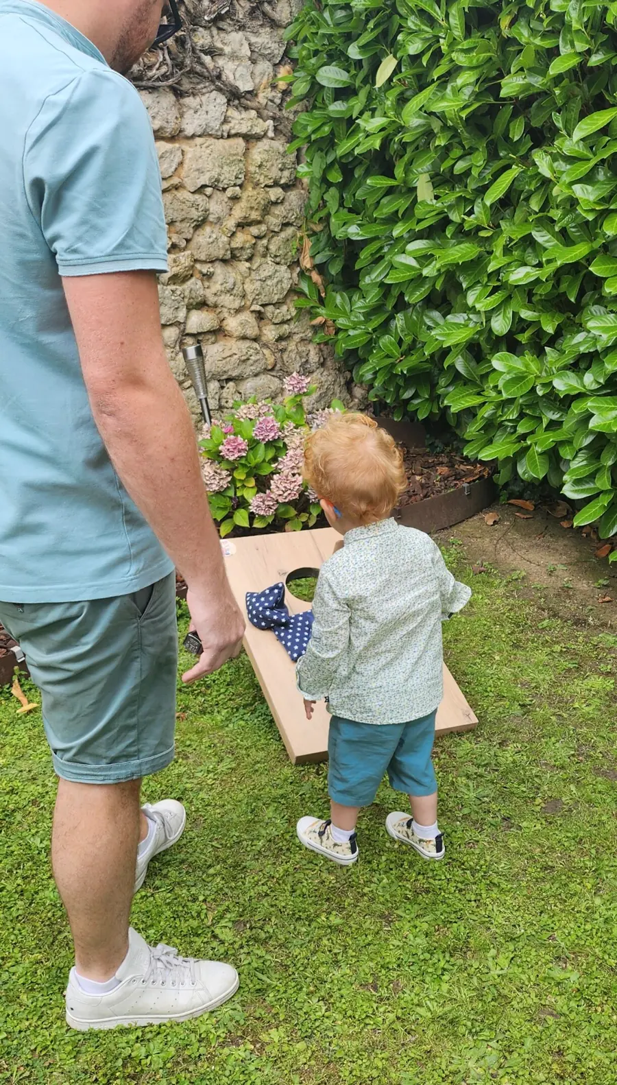 Dans un jardin, un père et son jeune fils jouent à un jeu de lancer en bois