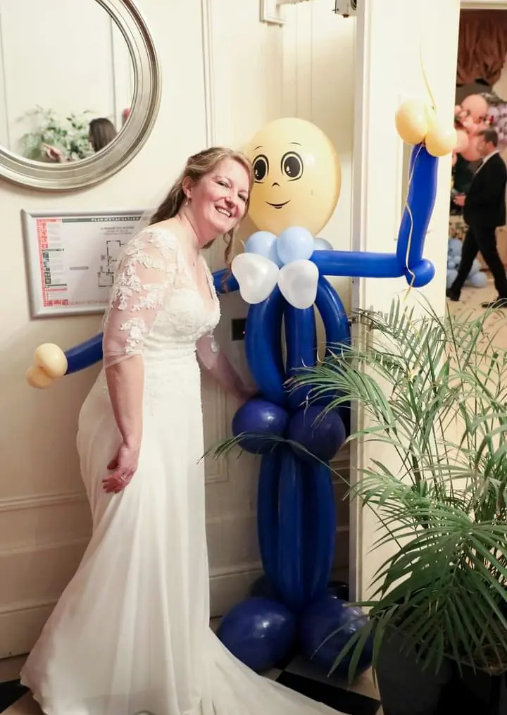 Une mariée pose à côté d’un grand personnage sculpté en ballons bleus