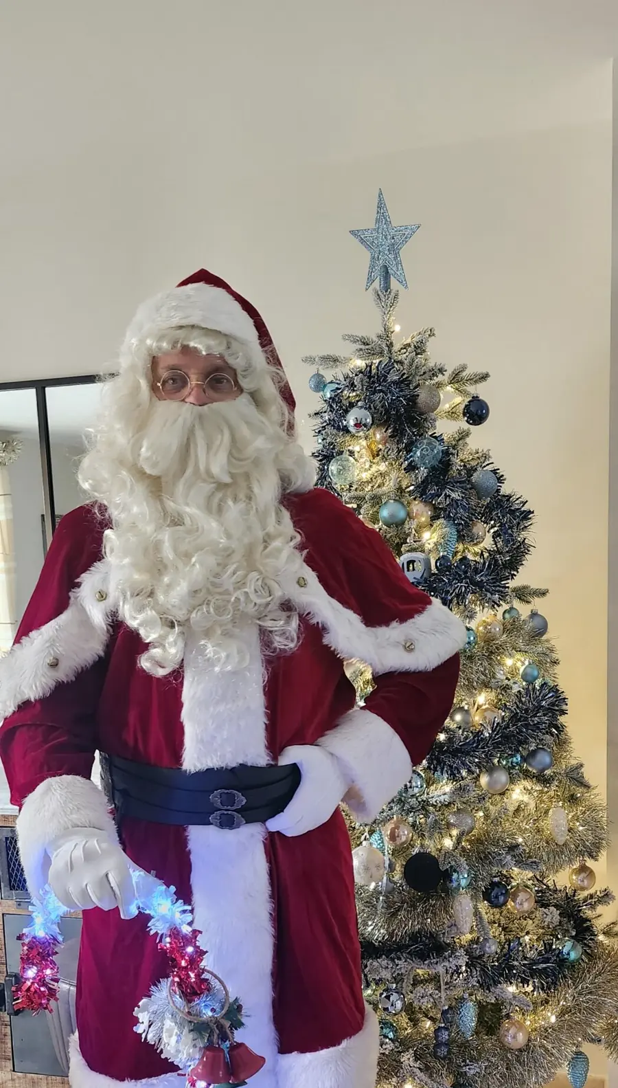 Le Père Noël à côté d’un sapin décoré, un sucre d’orge lumineux à la main